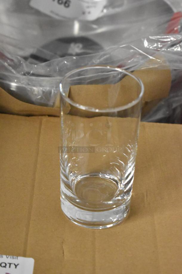 Clear glass tumbler, cylindrical shape, resting on a cardboard box. Appears to be in excellent condition.