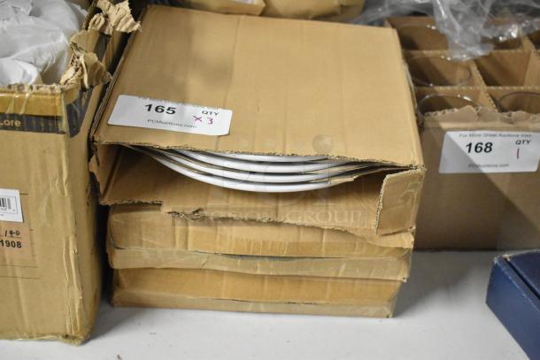 Cardboard boxes containing white plates, labeled "165 QTY x3" for auction, in storage condition.