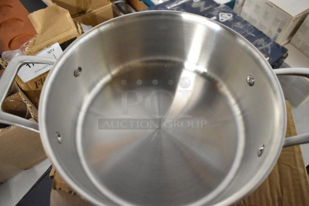 Stainless steel stockpot with riveted handles, in excellent condition, shown on a cardboard surface.
