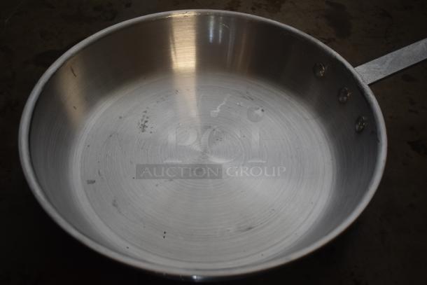 Stainless steel frying pan with riveted handle, showing light scratches and wear, suitable for professional use.