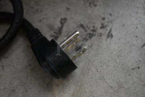Three-prong black electrical plug against concrete background, in good condition, no visible labels or markings.