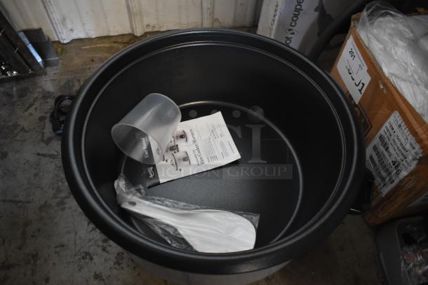 Large black rice cooker bowl with measuring cup, paddle, and instruction manual. Appears unused and in excellent condition.
