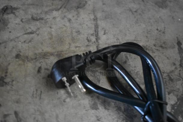 Black power cord with a two-prong plug, coiled on a concrete surface, showing slight wear.
