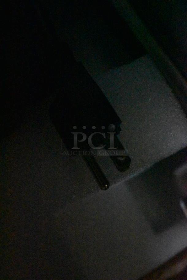 Close-up of a black electrical plug against a dark surface, showing two metal prongs. Condition appears used. No visible markings.