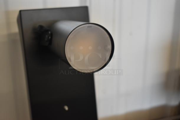 Black cylindrical LED spotlight fixture on a mounting bracket, matte finish, with adjustable angle. In excellent condition.