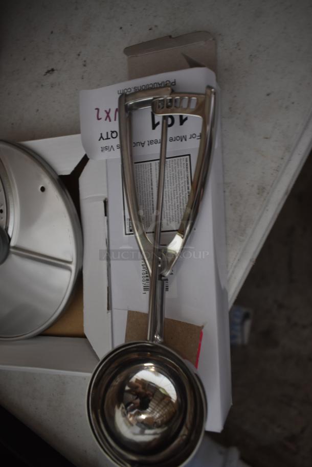 Stainless steel ice cream scoop with ergonomic handle, in excellent condition, atop packaging with barcode visible.