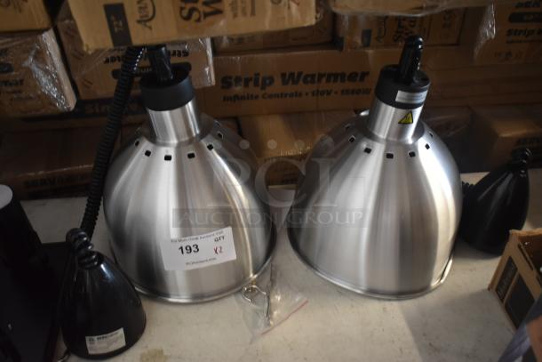 Two stainless steel heat lamps with coiled cords, shown on a table with cardboard boxes. Auction tag reads "193."