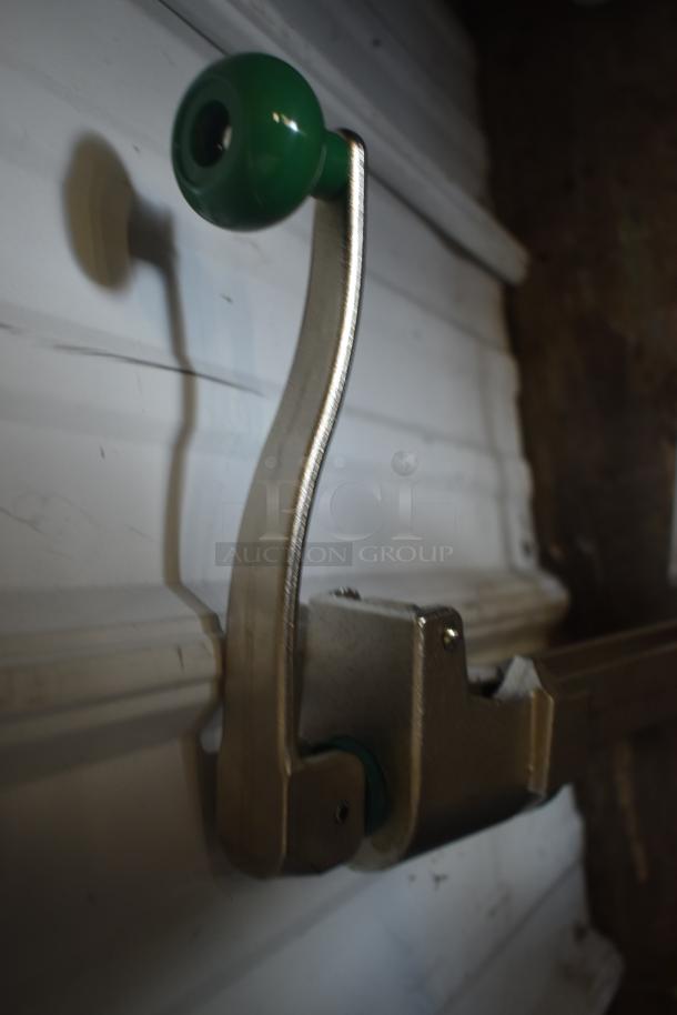 Metal lever with green plastic handle, mounted on a wall, slightly worn condition.