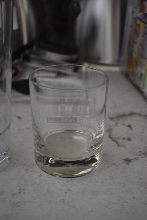 Clear glass tumbler on a textured surface, in used condition, with thick base, no visible markings or labels.