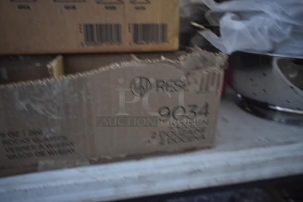 Damaged cardboard box labeled "RESE 9034." Contains 36-ounce rocks glasses. Box shows wear but remains closed.