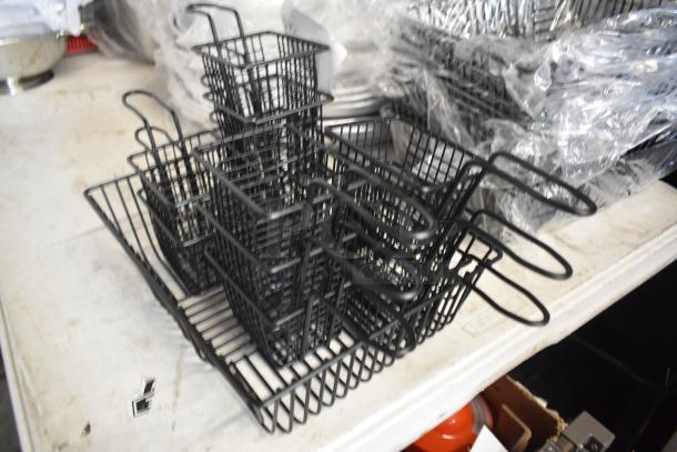 Stack of black metal fry baskets on a table, excellent condition, ideal for kitchen or restaurant use, various sizes visible.