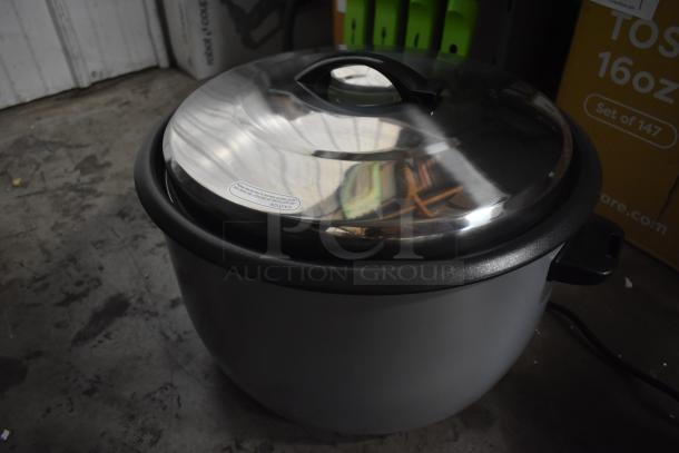 Large electric rice cooker with a stainless steel lid, black handle, and caution label. Appears in good condition.