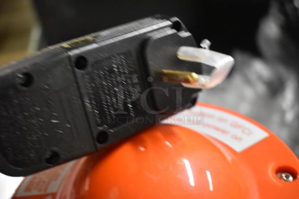 Close-up of a black electronic plug with gold prongs resting on a red surface, showing text and instructions.