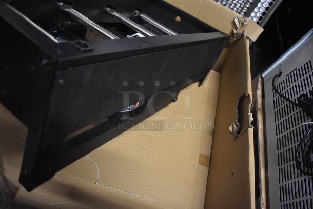 Black metal rack unit in partially opened box, showing minor wear. Cardboard box is torn. No visible labels or markings.