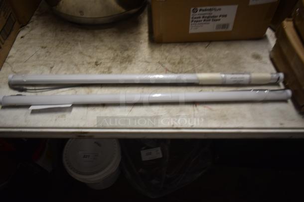 Two long cylindrical fluorescent light tubes, wrapped in plastic with wires exposed, on a workbench. Tags indicate type and model.