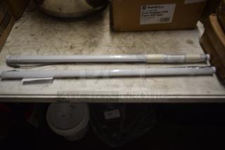 Two long cylindrical fluorescent light tubes, wrapped in plastic with wires exposed, on a workbench. Tags indicate type and model.