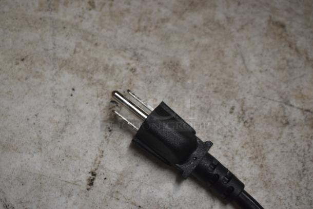 Black electrical plug with three metal prongs, shown on a textured surface, in good condition.