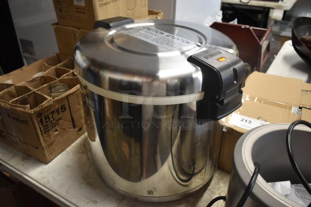 Stainless steel commercial rice cooker with caution label, black handles, and visible wiring, in used condition.