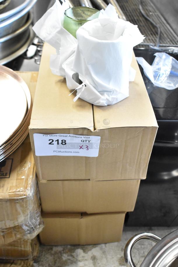 Stack of sealed boxes with an auction label marked "218 QTY 3." Wrapped glassware on top, in new condition.
