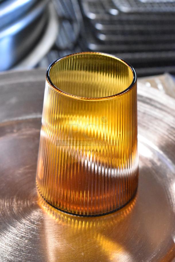 Amber ribbed glass vase with vertical grooves, in excellent condition, set on a metallic surface.