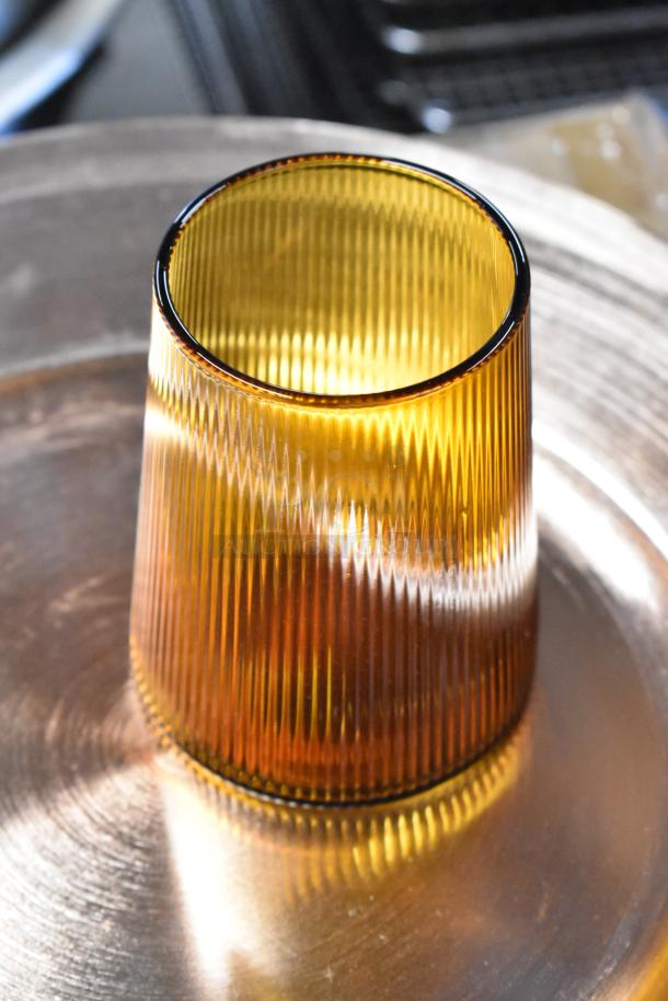 Amber ribbed glass tumbler, cylindrical shape, excellent condition, reflective surface, no visible markings, 4-inch height.