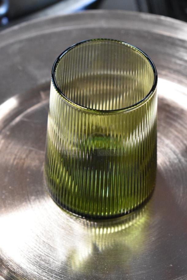 Green ribbed glass tumbler on metallic surface, excellent condition.