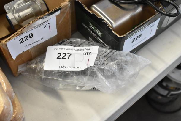 Plastic-wrapped item labeled "227" beside a Garde electric knife sharpener and metal component. Auction organized by PClAuctions.com.