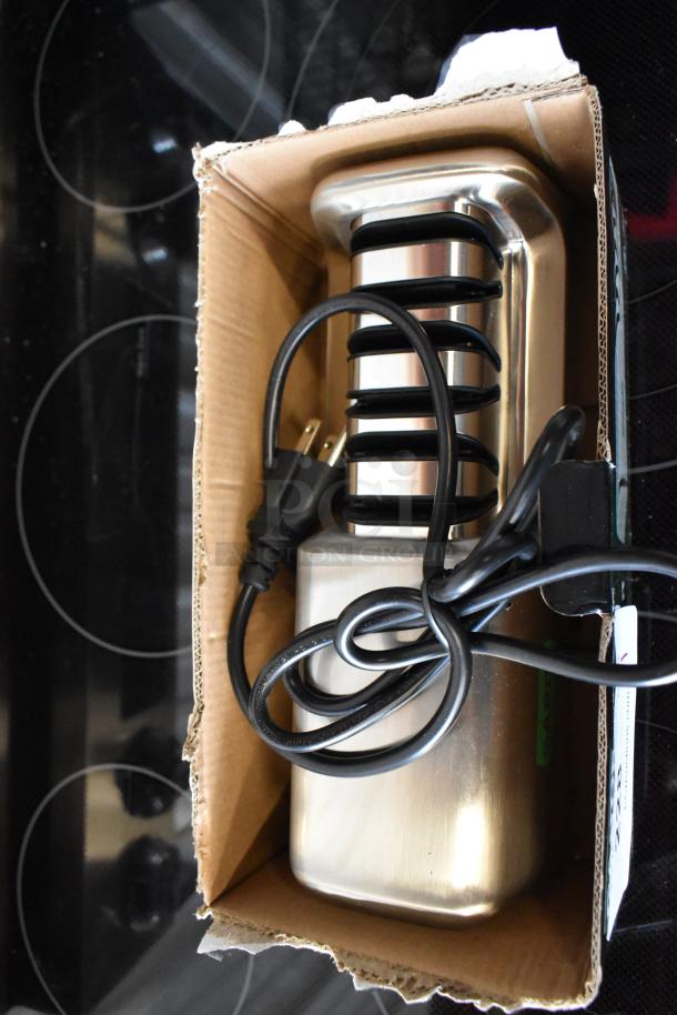 Stainless steel electric bread slicer in original packaging, unused condition, with power cord and black safety grill.