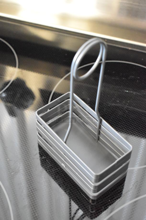 Silver metal basket with a handle, on a glass stovetop. Rectangular with parallel slats. Appears in new condition.