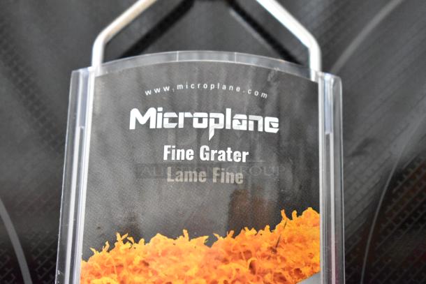 Microplane fine grater with handle, labeled "Lame Fine." Features sharp, fine grating surface. Brand and website visible.