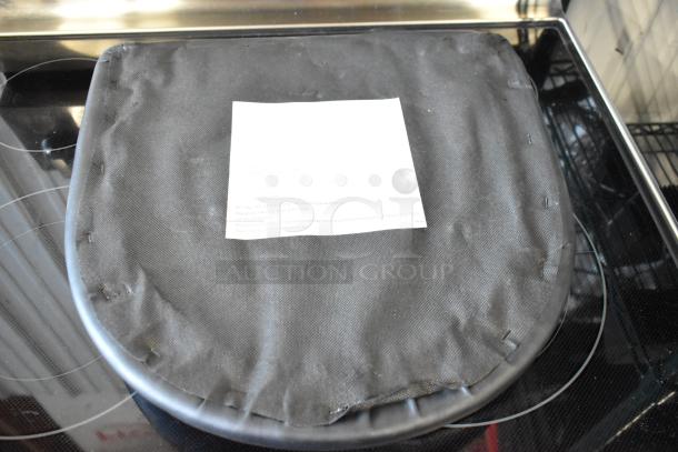 Black padded seat cushion with fabric cover and visible tag. The tag includes manufacturing details and compliance information.