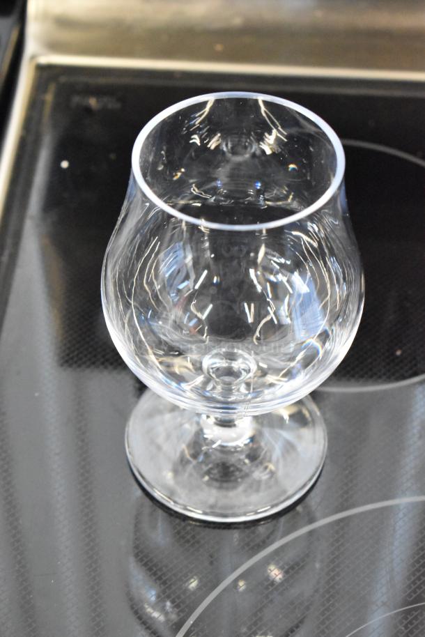 Clear stemmed brandy snifter glass with a wide bowl, in excellent condition, displayed on a glass surface.