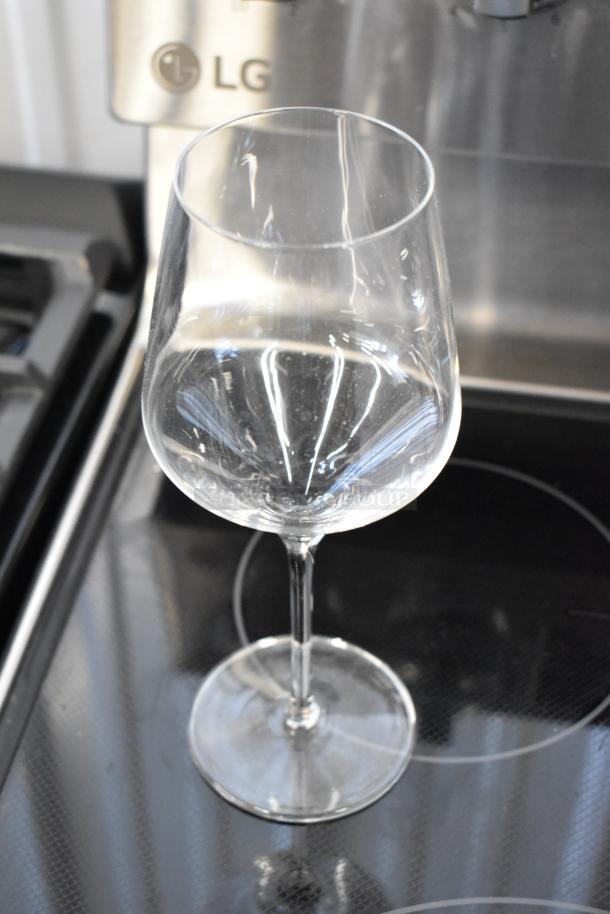 Clear wine glass with a long stem, reflective surface, and no visible imperfections. Set on a stovetop.