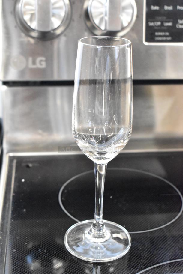 Elegant clear glass champagne flute, pristine condition, with a simple design and tall stem, displayed on a stove.