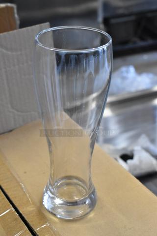 Clear glass beer glass, tall with a wide mouth and sturdy base, in excellent condition, placed on cardboard.