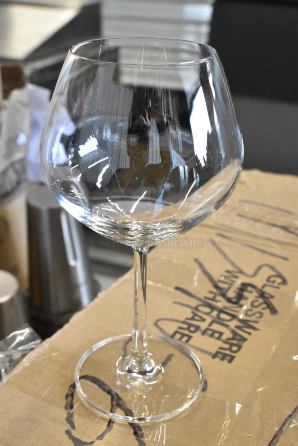 Clear crystal wine glass with a wide bowl, long stem, and round base, in excellent condition. Set on a cardboard surface.