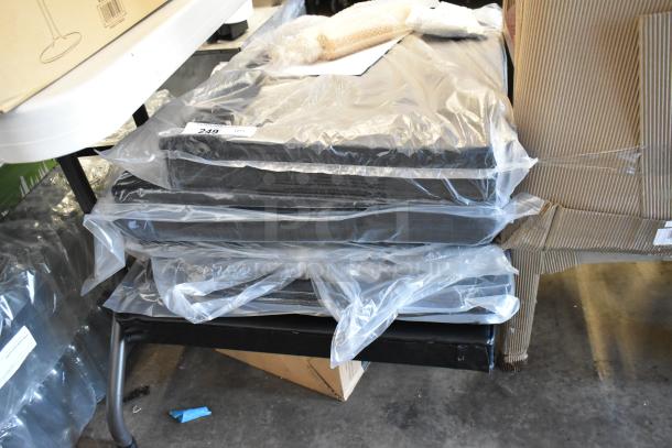 Stack of black cushioned seats in plastic wrapping, numbered tag 249 visible. New condition under a table.