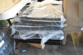 Stack of black cushioned seats in plastic wrapping, numbered tag 249 visible. New condition under a table.