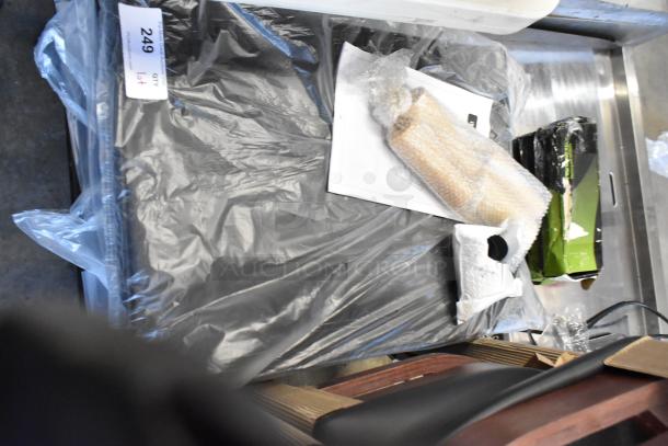 Plastic-wrapped package with auction tag labeled "249" on a metal surface, includes bubble-wrapped items and box. Condition unknown.