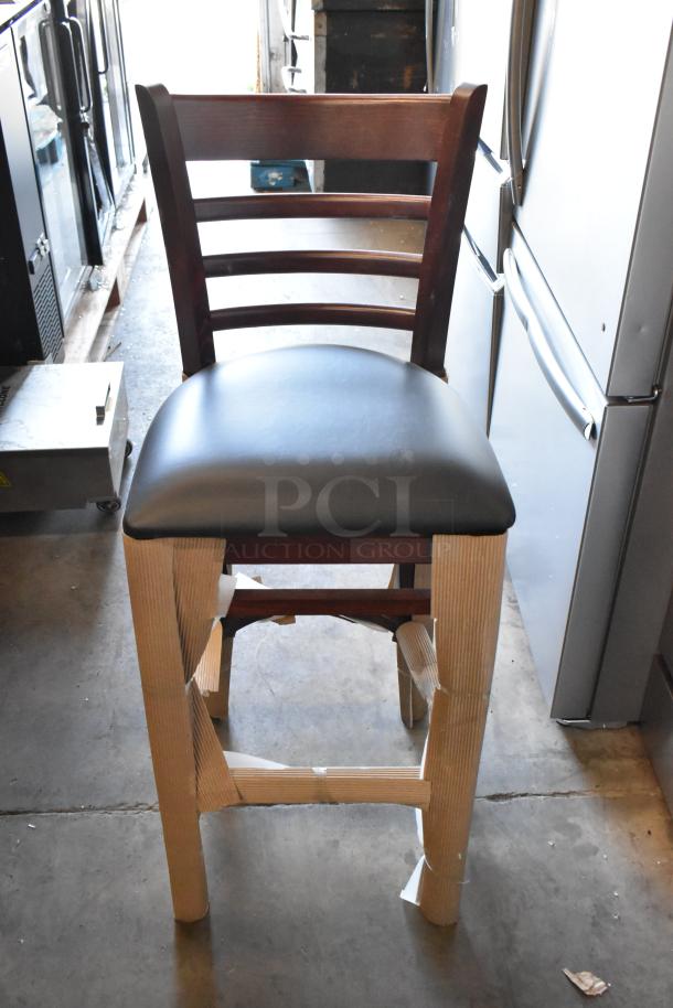 Wooden bar stool with dark brown finish and black cushioned seat, packaging on legs, like-new condition.