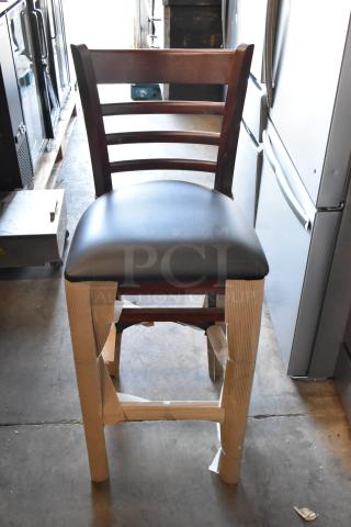 Wooden bar stool with dark brown finish and black cushioned seat, packaging on legs, like-new condition.
