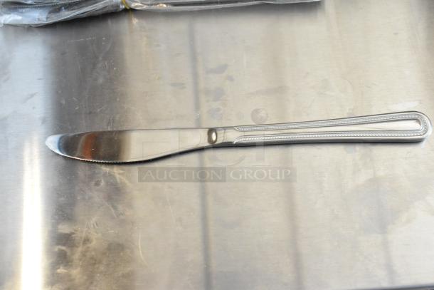 Stainless steel dinner knife with a serrated edge and beaded handle design, in excellent condition on a metal surface.