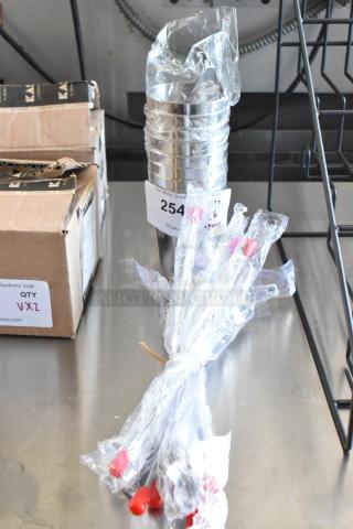 Industrial tubing with red caps wrapped in plastic, labeled "254" and "6 spoons," next to a cardboard box with "QTY V2" tag.