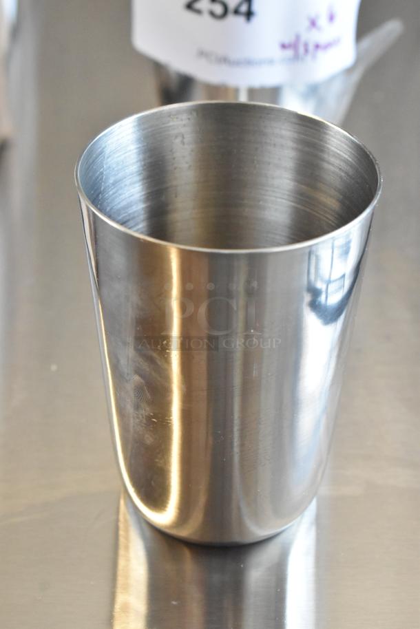 Stainless steel cup, glossy finish, cylindrical shape. Auction tag reading "254" in background. Ideal for beverages.