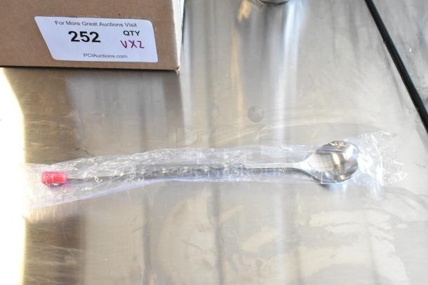 Stainless steel spoon in clear packaging with a red cap, new condition. Box label reads "252 QTY VXZ," from PCIAuctions.com.