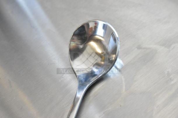 Stainless steel spoon with a wide, rounded bowl on a plain metal surface, in good condition, no visible markings.
