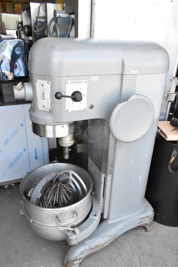 Hobart industrial mixer with metal bowl and whisk attachment, in used condition. Model label visible, showing speed settings.