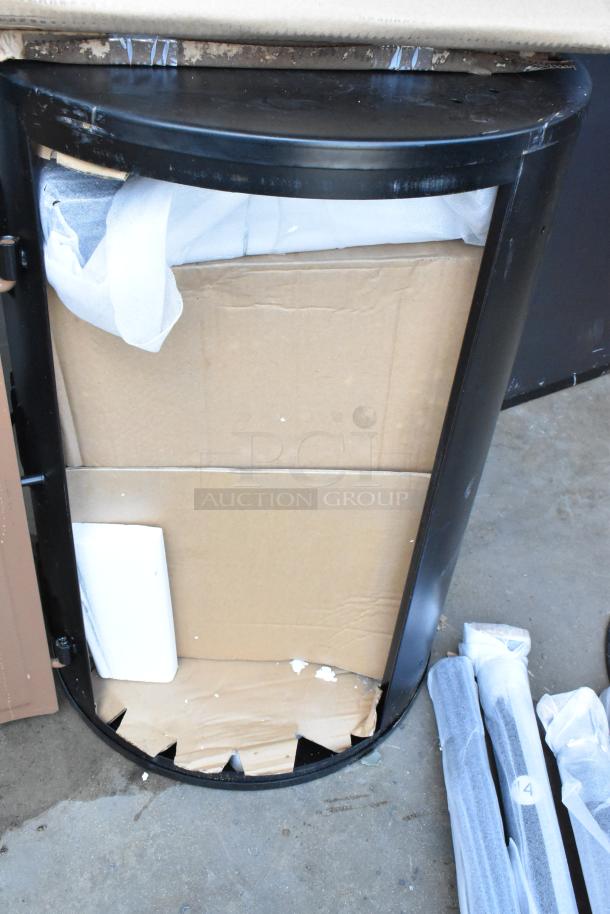 Black metal half-circle desk frame, partially assembled, with cardboard and packaging materials. Possible scratches visible.
