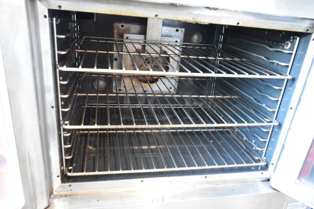 Commercial convection oven interior, three metal racks, used condition, visible wear on back panel, stainless steel frame.