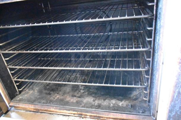 Commercial oven interior with four metal racks, showing wear and discoloration. Suitable for large capacity cooking.